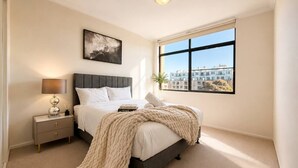 Una camera da letto con un letto, un comodino, una lampada e una finestra con vista sulla città.