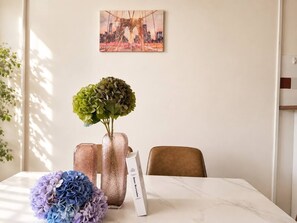 Et spisebord med to vaser, hvoraf den ene indeholder grønt løv og den anden blå blomster, samt en bog med titlen 'Anecdotal'.