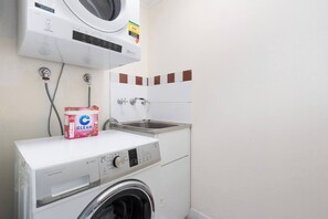 Ein kleiner Waschbereich mit einer Waschmaschine mit Frontlader, einem Trockner und einem Spülbecken.