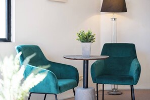 Ein Zimmer mit Türkis-farbenen Stühlen, einem kleinen runden Tisch mit Topfpflanze und einer Stehlampe.