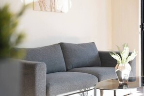 En moderne stue med en grå sofa, et glasbord og en potteplante.