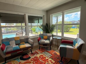 Un solarium con vista a la piscina, dos sillas con cojines estampados, una mesita y una planta grande.