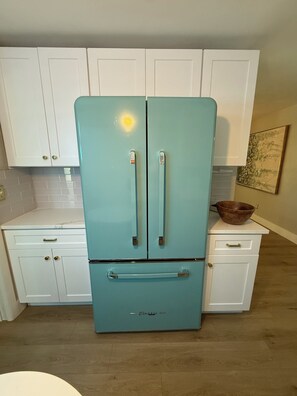 A kitchen with a teal-colored refrigerator, white cabinets, and a wooden floor. - Retro styled paradise 3bed/2br Cape Coral pool home on the canal front (Cape Coral)