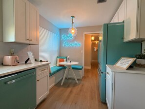 A compact kitchen with a neon sign, a dining area with a small table, and a refrigerator. - Retro styled paradise 3bed/2br Cape Coral pool home on the canal front (Cape Coral)