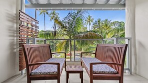 Ein Balkon mit zwei Holzstühlen und einem kleinen Tisch, Blick auf Palmen und einen klaren Himmel.