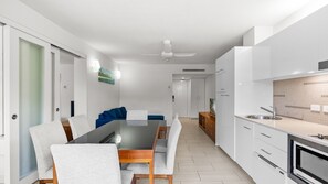 A modern kitchen with white cabinets, a dining area with a glass table, and a blue sofa. - Palm Cove Apartment with Resort Pool, Gym and Parking | 2308 Drift (Palm Cove)