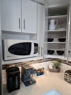 A kitchen with white cabinets, a microwave, a coffee maker, and a toaster. - Near WEM | Entire Home+Full AC+Sleeps8+FreeParking (Edmonton)