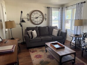 Un salon avec un canapé, une table basse, une horloge et une lampe.