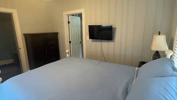 A bedroom with a bed, a ceiling fan, a television, and a door.