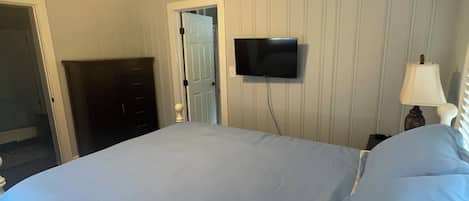 A bedroom with a bed, a ceiling fan, a television, and a door.