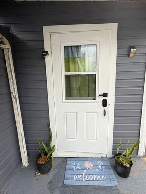 A white door with a window, a doorbell, and a welcome mat. - Starfish Cove- Grand Cayman (Grand Cayman)