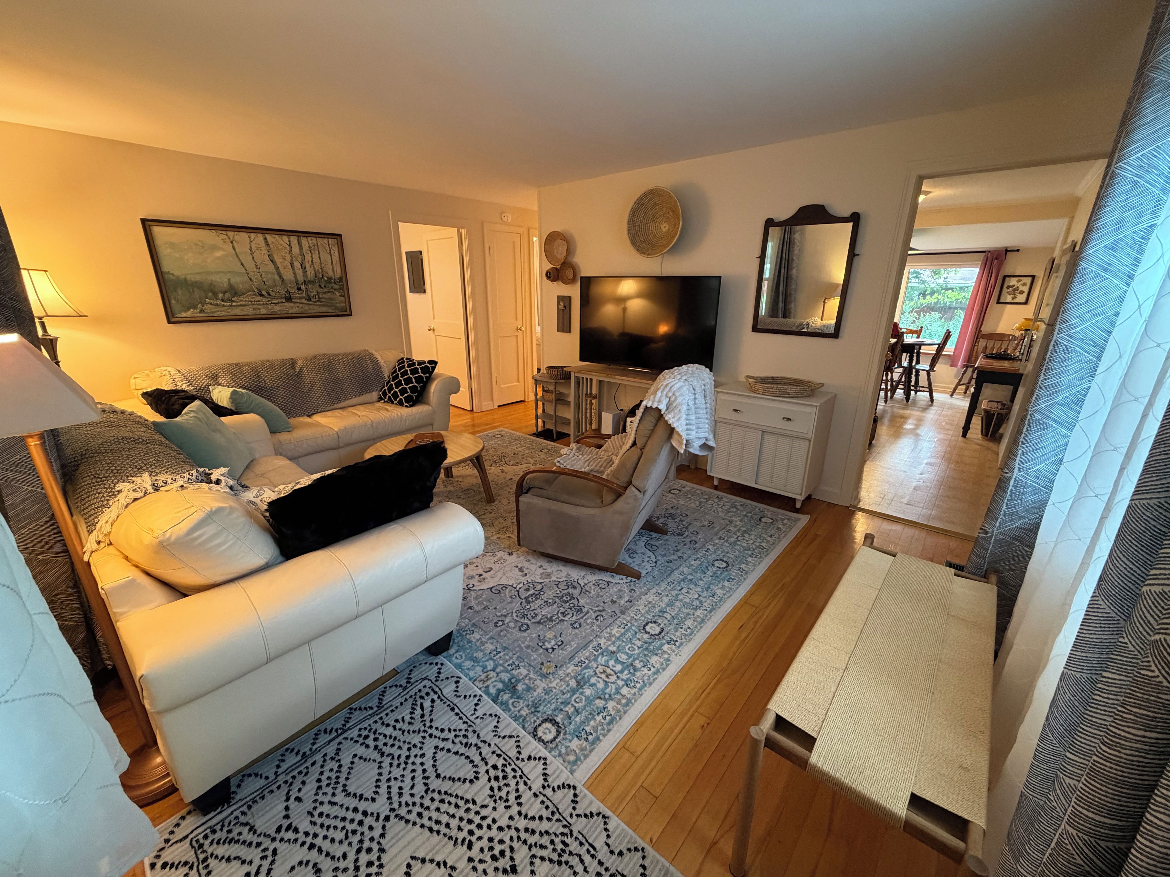 A living room with a sofa, armchair, TV, and a dining area in the background.