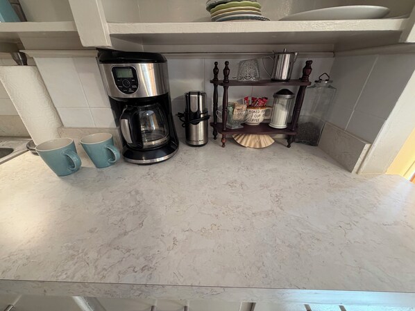 A kitchen with a coffee maker, two mugs, a shelf with kitchenware, and a tiled backsplash. - Cozy home minutes from SU campus, area hospitals & all major highways. (Syracuse)