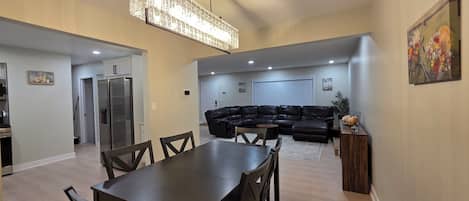 Un salon moderne avec un canapé d’angle, une table à manger avec des chaises et un lustre.