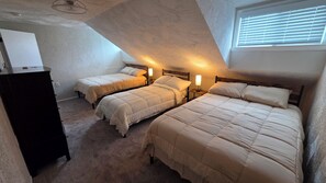Ein Zimmer mit drei Betten, die in einer Ecke angeordnet sind, jeweils mit Nachttisch und Lampe.