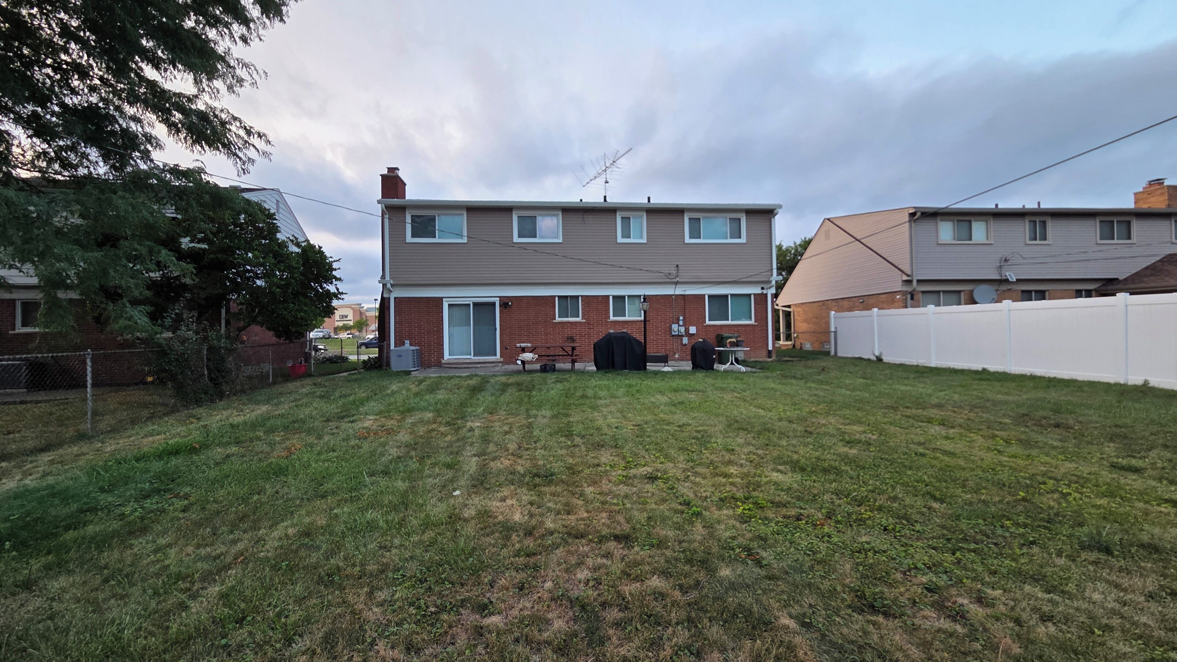 A two-story residential building with a front yard, a barbecue grill, and a white fence.