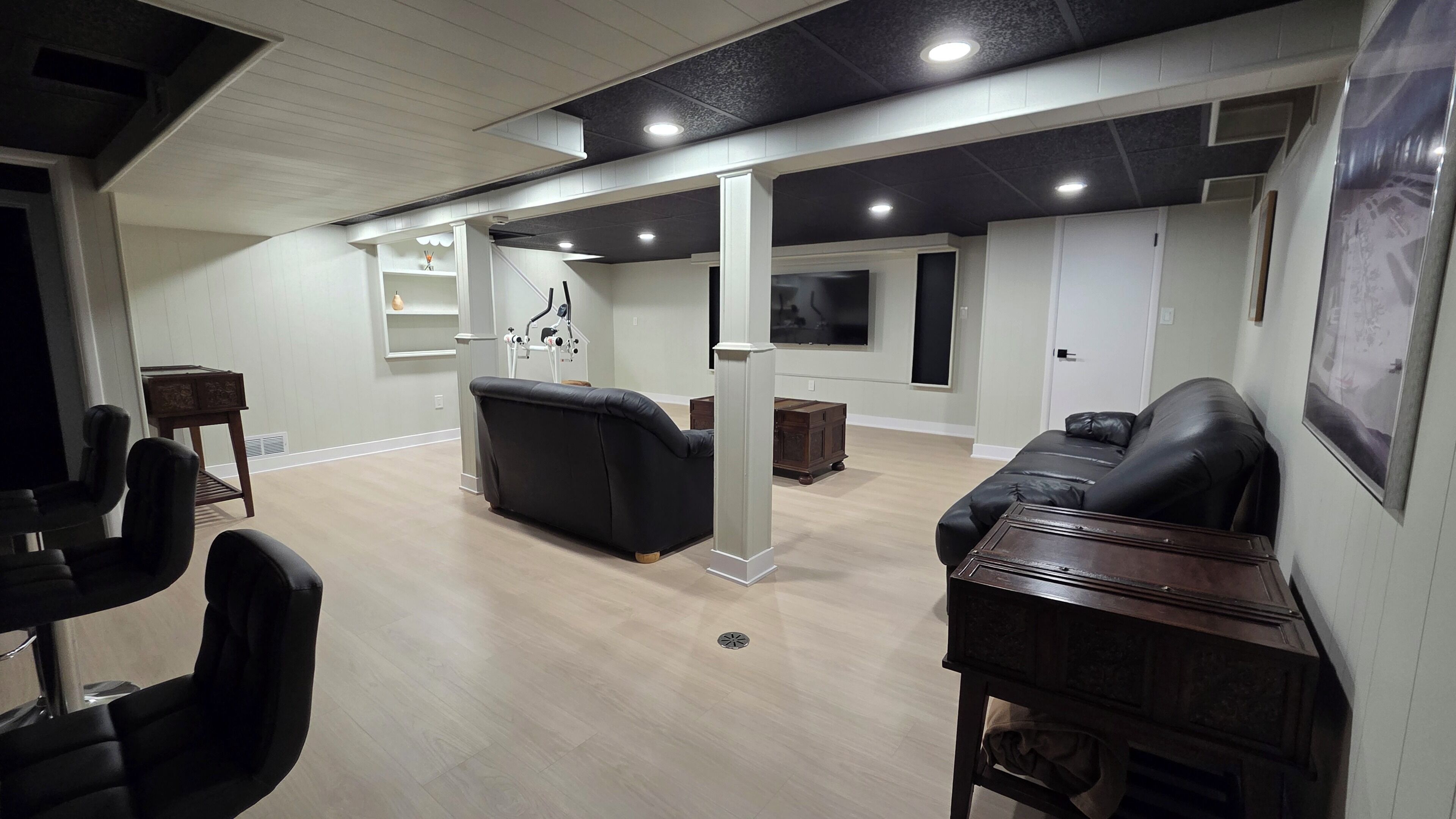 A spacious room with a black leather sofa, a wooden cabinet, and a television mounted on the wall.