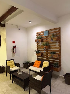 Un vestíbulo con mobiliario de mimbre, una pared vegetal de madera y un extintor.