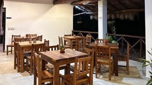 Un comedor interior con mesas y sillas de madera, techo de paja y vistas al cielo nocturno.