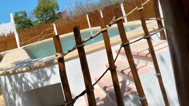 Zona de piscina con una barrera de cuerda, una estructura de concreto y un cielo azul claro.