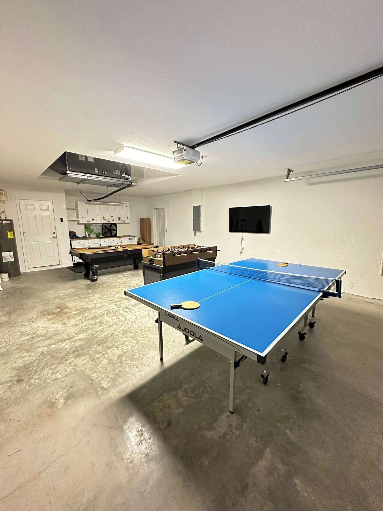 A room with a ping pong table, a foosball table, and a projector mounted on the ceiling.