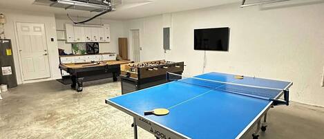 A room with a ping pong table, a foosball table, and a projector mounted on the ceiling.