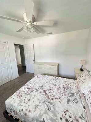 Un dormitorio con cama, cómoda, mesita de noche, ventilador de techo y puerta que da a otra habitación.