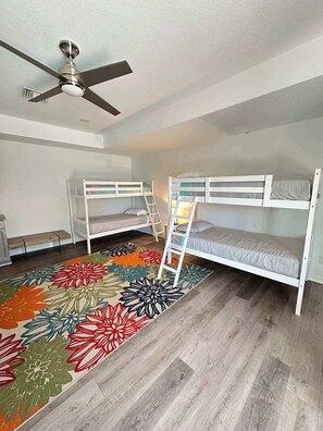 A room with two bunk beds, a ceiling fan, a bench, and a floral-patterned rug. - Villa Seashell - Cape Coral (Cape Coral)