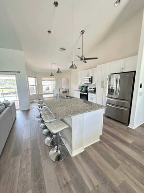 A modern kitchen with a central island, stainless steel appliances, and a bar seating area. - Villa Seashell - Cape Coral (Cape Coral)