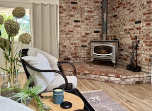 Una habitación acogedora con pared de ladrillo, un sofá blanco, una mesita con un florero de plantas y un estufa de leña.