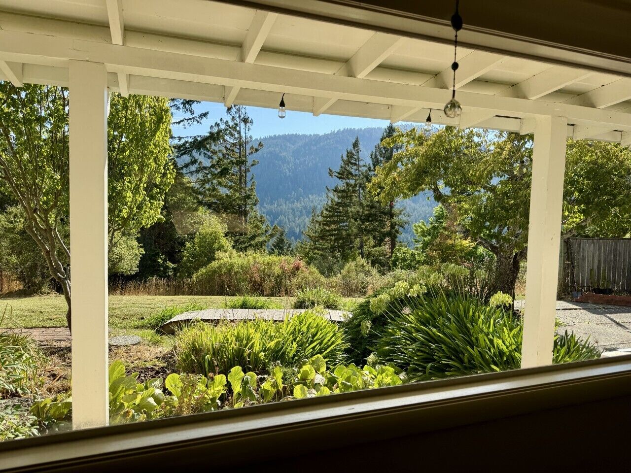 A covered patio with a view of a landscaped garden and mountains.