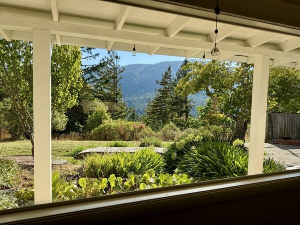A covered patio with a view of a landscaped garden and mountains.