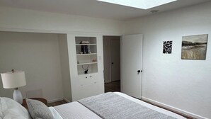 Une chambre à coucher comprenant un lit, une table de chevet, une lampe, une armoire et une œuvre d’art accrochée au mur.