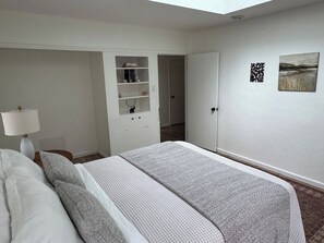 A bedroom with a bed, bedside table, lamp, wardrobe, and artwork on the wall.