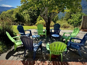 An outdoor seating area with chairs arranged around a central table, surrounded by trees and a mountainous backdrop.