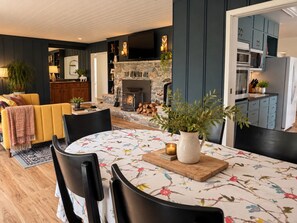 A modern kitchen with a stone fireplace, a dining area with a floral tablecloth, and a cozy living space with a yellow sofa.