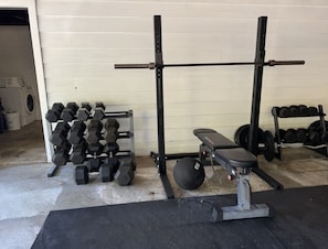 A gym with weightlifting equipment, including dumbbells, a bench, and a barbell.