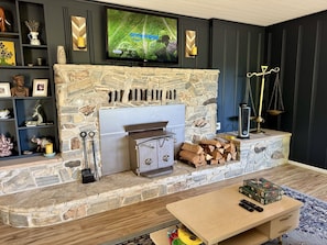 Una sala de estar con chimenea de piedra, un televisor montado encima y una mesa de centro con juegos de mesa.