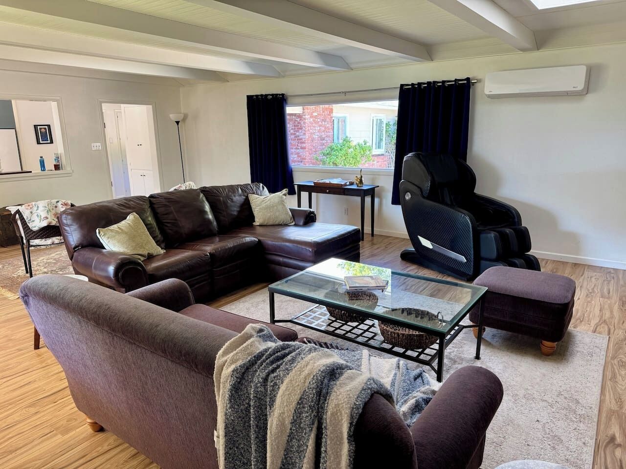 A living room with a leather sofa, a glass coffee table, and a black office chair.