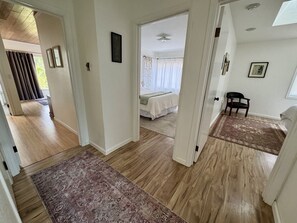 Un pasillo que conduce a un dormitorio con cama, una silla y una alfombra.