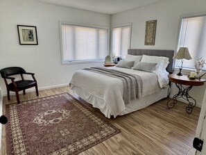 A bedroom with a bed, a chair, a bedside table, and a window with blinds.