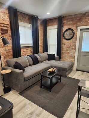 A modern living room with a grey sectional sofa, a black coffee table, and a brick wall. - Cozy 1-bedroom apartment in Beautiful Salt Lake City with W&D (Salt Lake City)