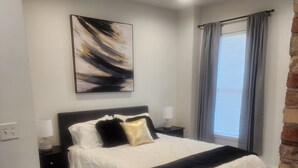 A bedroom with a bed, a nightstand, a lamp, a window with curtains, and a painting on the wall. - Cozy 1-bedroom apartment in Beautiful Salt Lake City with W&D (Salt Lake City)