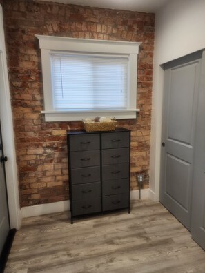 A room with a brick wall, a window with blinds, a black cabinet with drawers, and a gray door. - Cozy 1-bedroom apartment in Beautiful Salt Lake City with W&D (Salt Lake City)