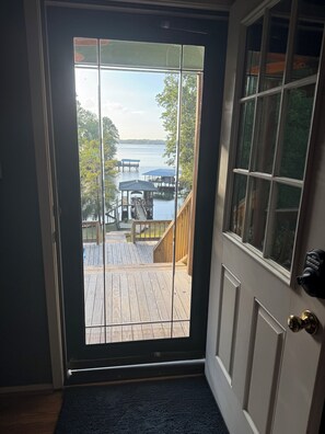 Visão através de uma porta de vidro para um deck de madeira com um píer que se estende sobre a água.