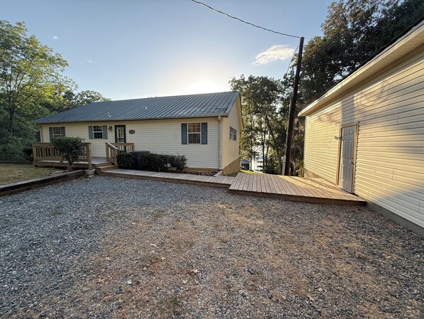 A two-story house with a front porch, a gravel driveway, and a wooden deck. - A Charming 3-bedroom house on Toledo Bend lake with garage and boat house (Many)