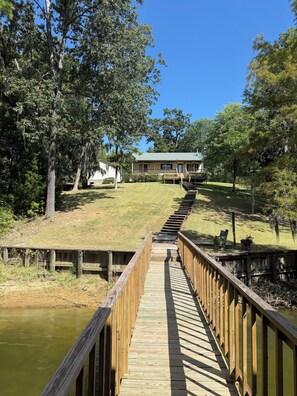 A wooden boardwalk leading to a building with a green roof, surrounded by trees and a grassy area. -  A Charming  3-bedroom house on Toledo Bend lake with garage and boat house (Many)