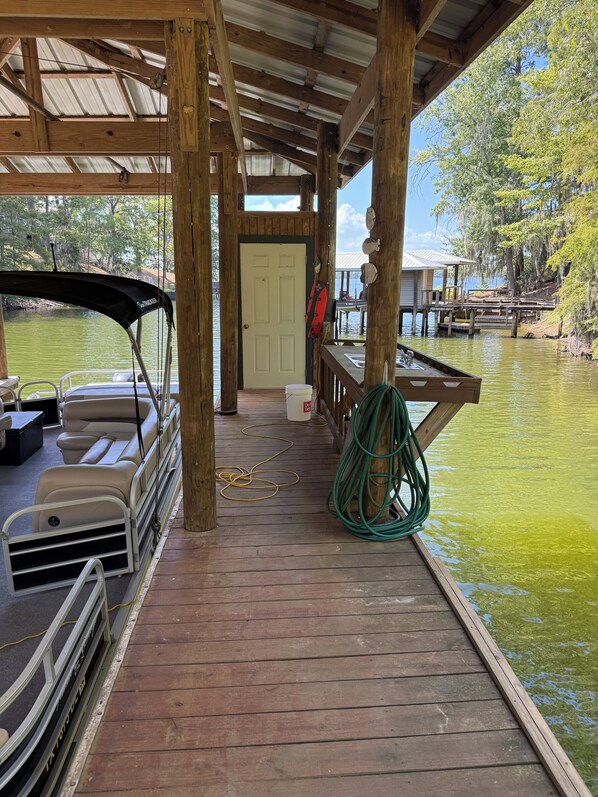 Um cais coberto com um barco, uma mangueira de jardim verde e um balde branco.