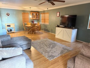 A living room with a grey sofa, a TV on a white cabinet, and a dining area with a wooden table and chairs. -  A Charming  3-bedroom house on Toledo Bend lake with garage and boat house (Many)