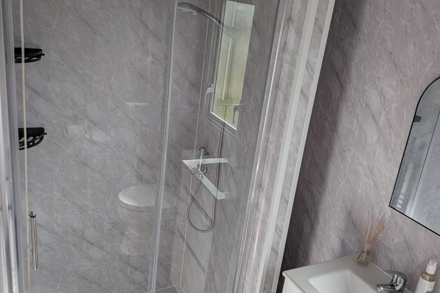Une salle de bain moderne avec une douche à parois de verre, un lavabo blanc et un mur en marbre.